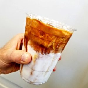 Close up of an iced coffee in a person's hand from Nexus Coffee Company.