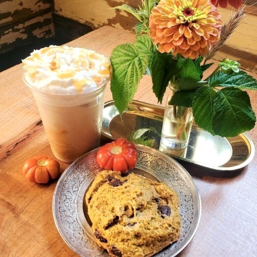 Pumpkin pie iced latte and a pumpkin chocolate scone sitting on a table with a vase of orange flowers.