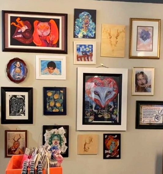 Many pieces of framed artwork hanging on a wall.