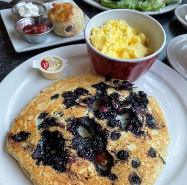 Plate with a huge blueberry pancake and a side of scrambled eggs.