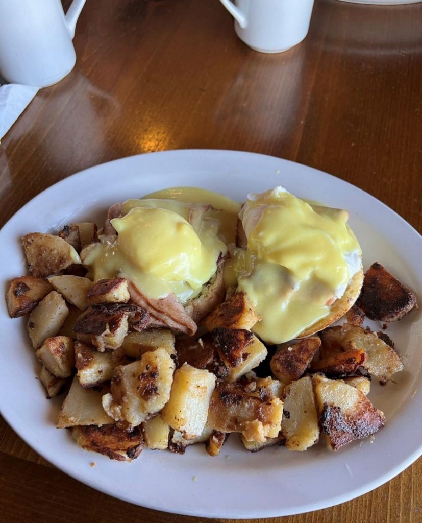Eggs benedict and home fries on a plate.