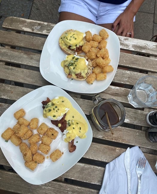 Overhead shot of a patio table with two plates of eggs benedict and tater tots.