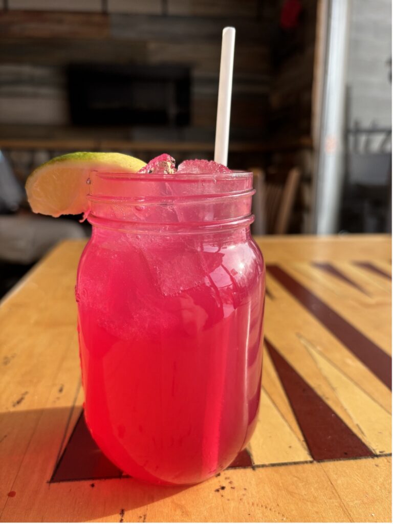 Bright pink drink with a lime wedge and a straw in a mason jar.