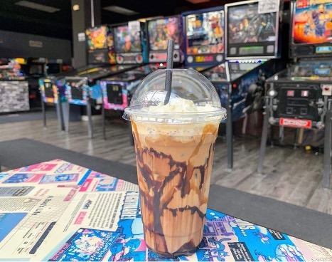 Close up of an iced coffee beverage from 8-bit Beans in Whitby with arcade games in the background.