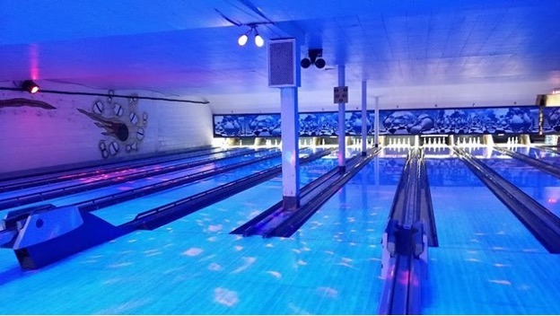 Low lit bowling alley lanes with blue and pink lights.