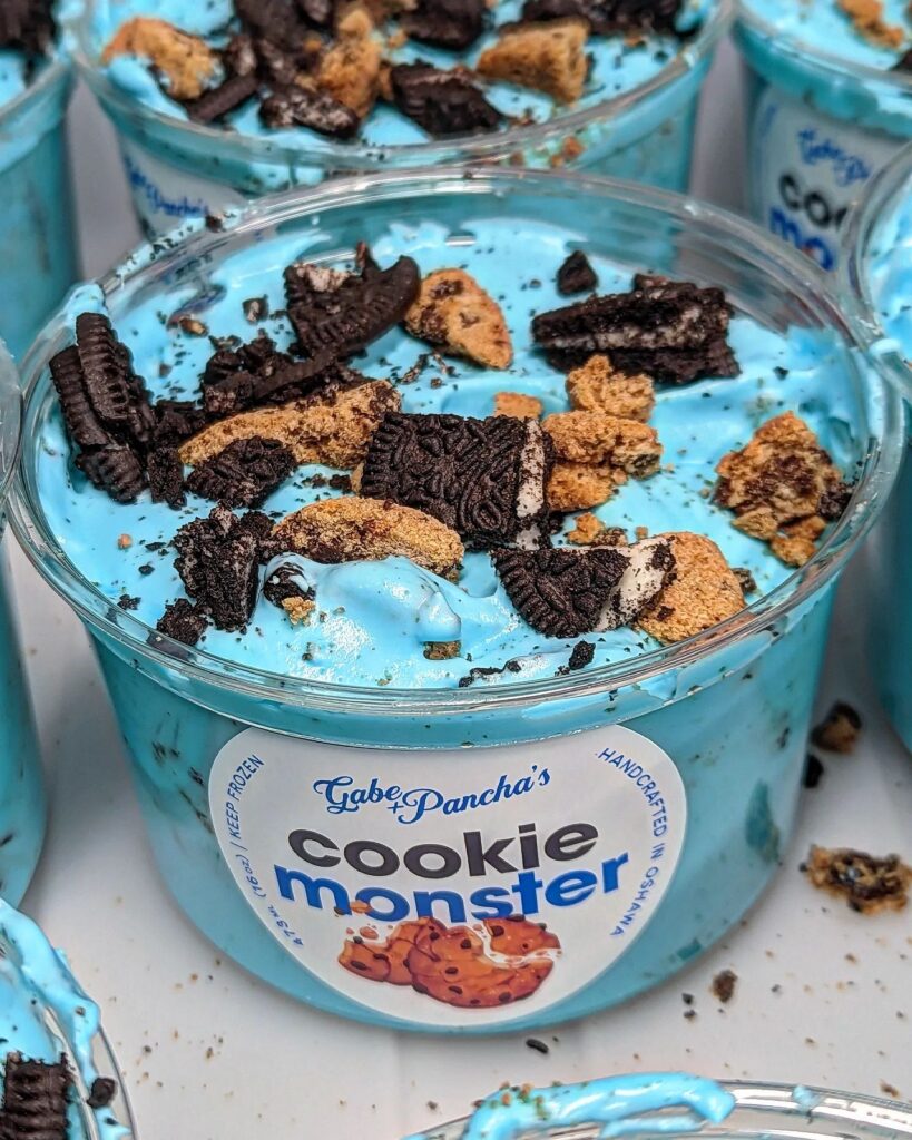 Close up of blue "cookie monster" ice cream in a cup with chunks of cookies on top.