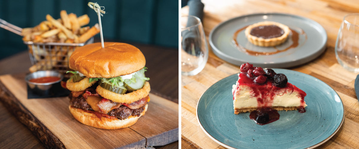 A close up of a burger and fries on a stylish wooden board and a berry cheesecake slice on a plate with a butter tart in the background.